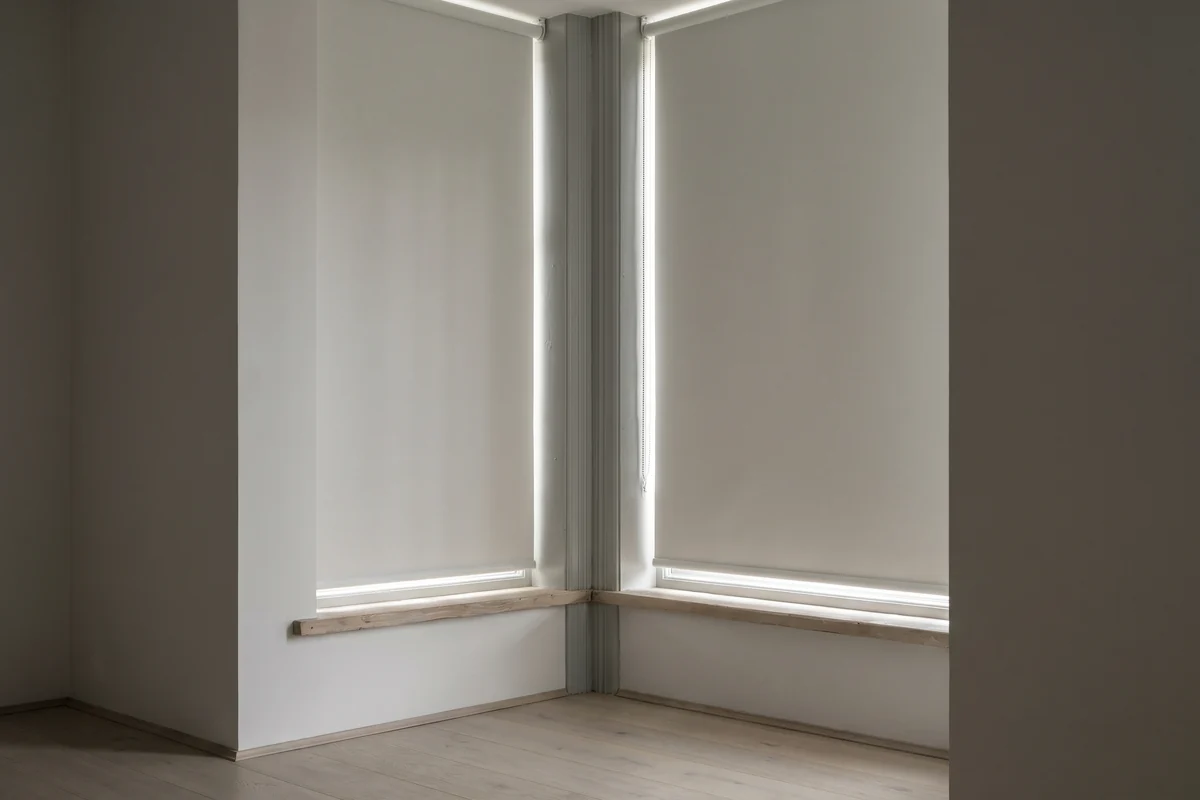 Two roller blinds meeting at the angled corner post of a bay, a thin strip of light down the join