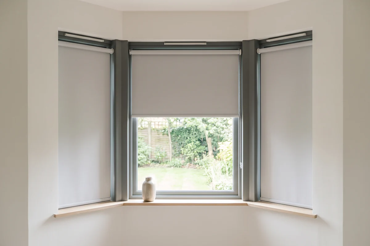 A three-sided bay window with a separate roller blind in each pane, the centre half raised and the sides lowered