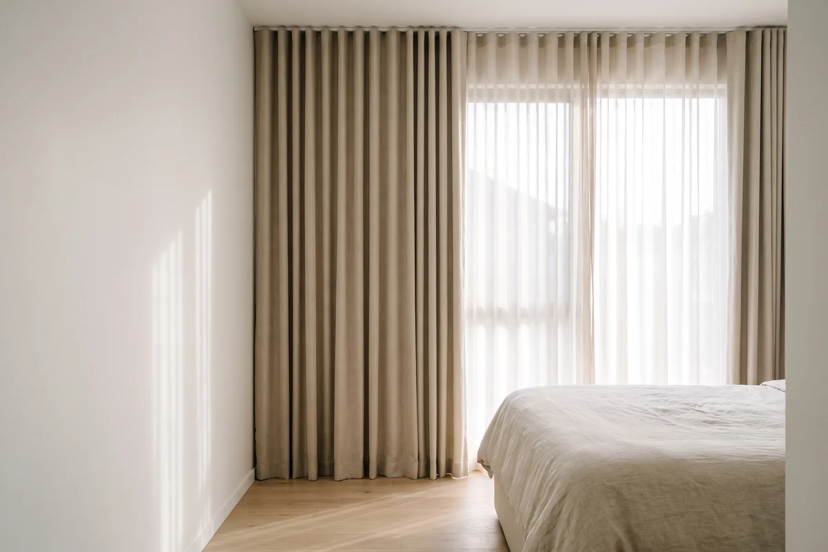 Pleated curtains hanging in even folds in a neutral bedroom