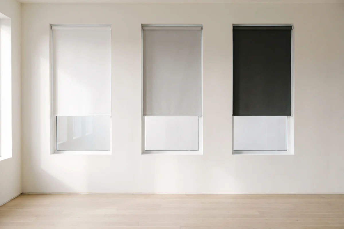 Three roller blinds in white, light grey and charcoal side by side across three windows