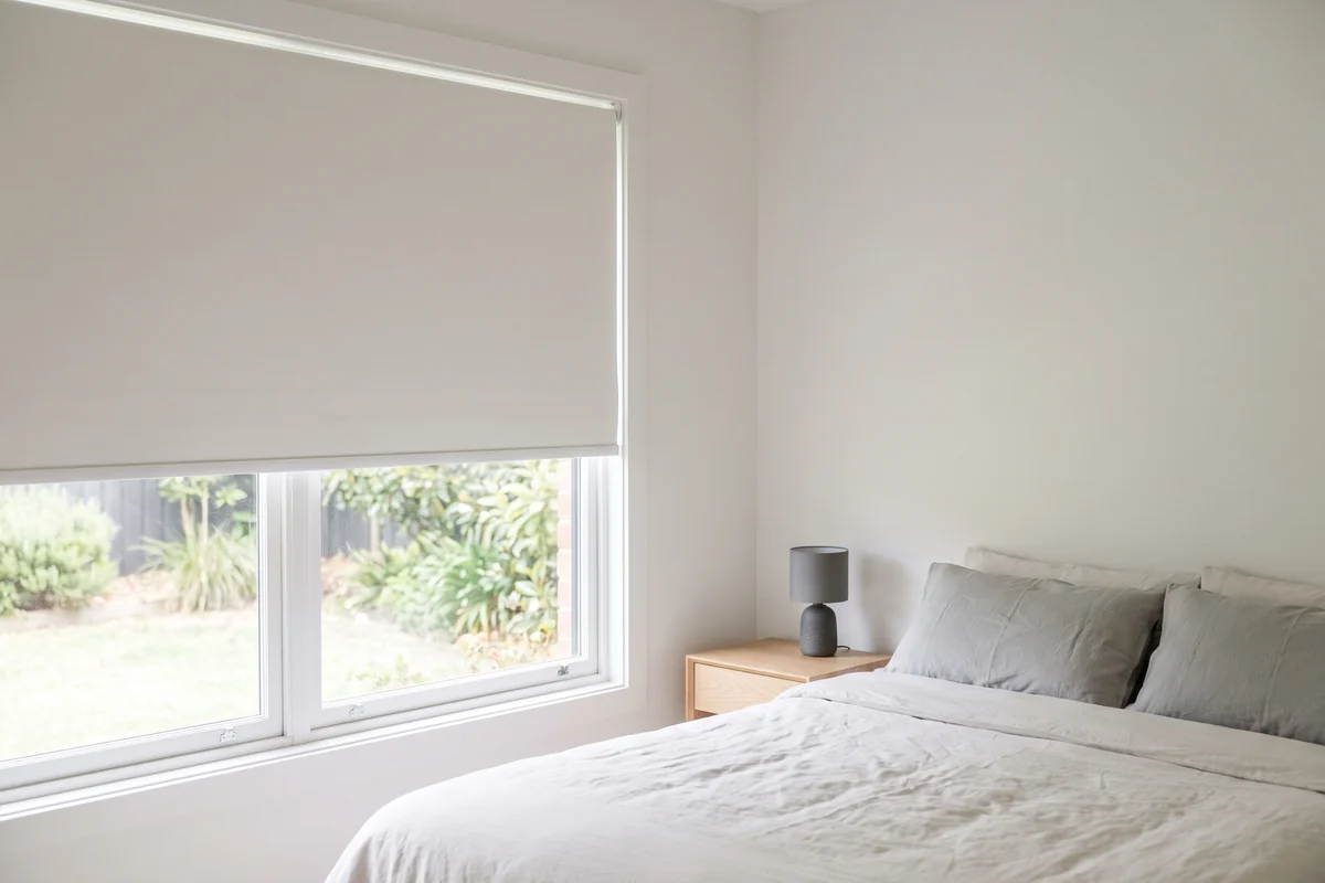 A plain white roller blind in good order, half lowered at a bedroom window