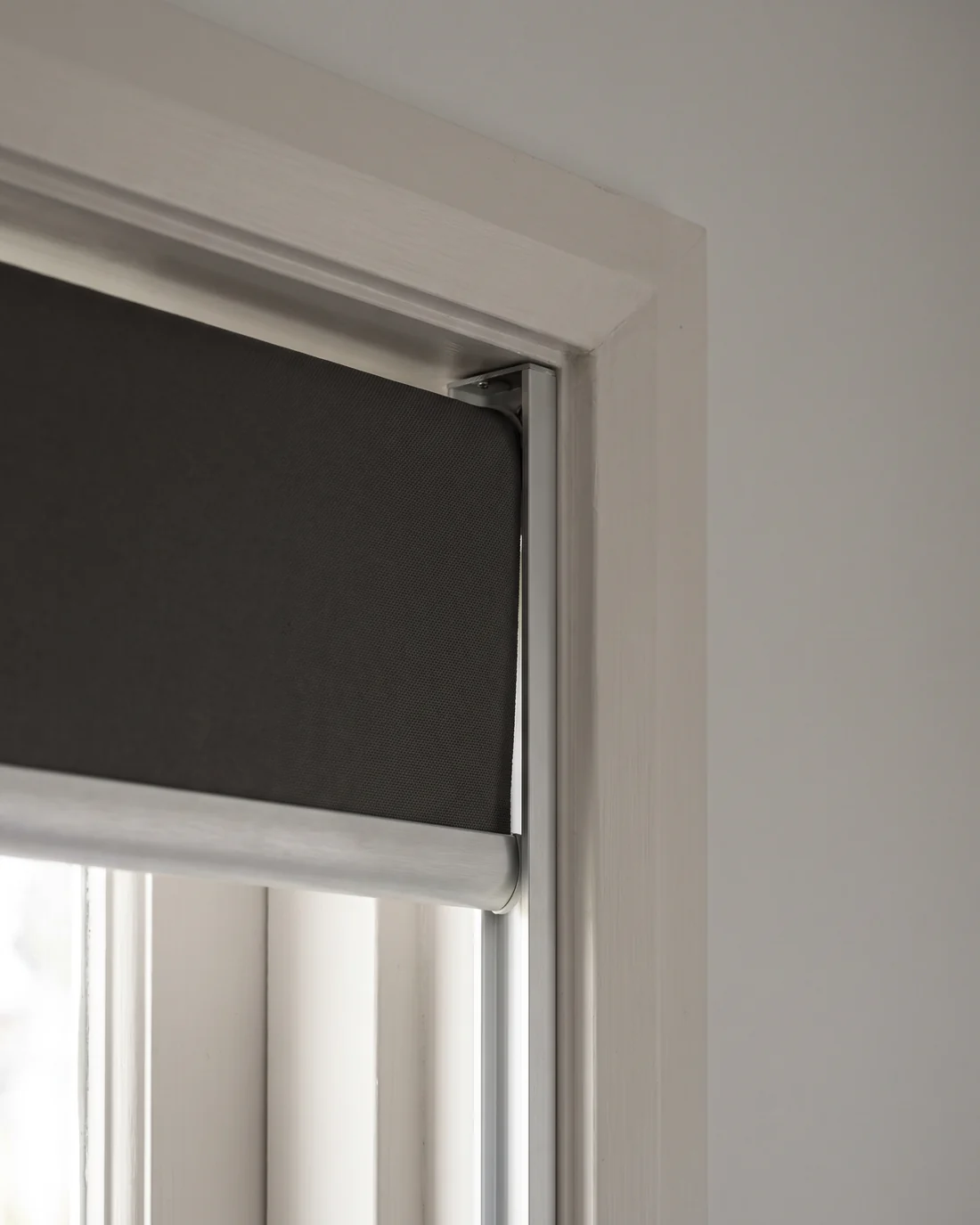 The edge of a blockout roller blind running inside an aluminium side channel fixed to the architrave