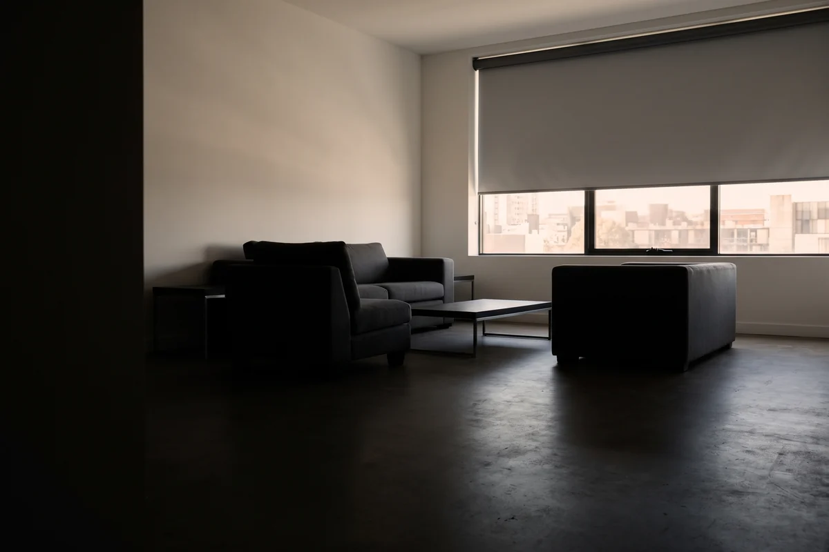 A blockout roller blind half drawn across a wide living-room window in afternoon light