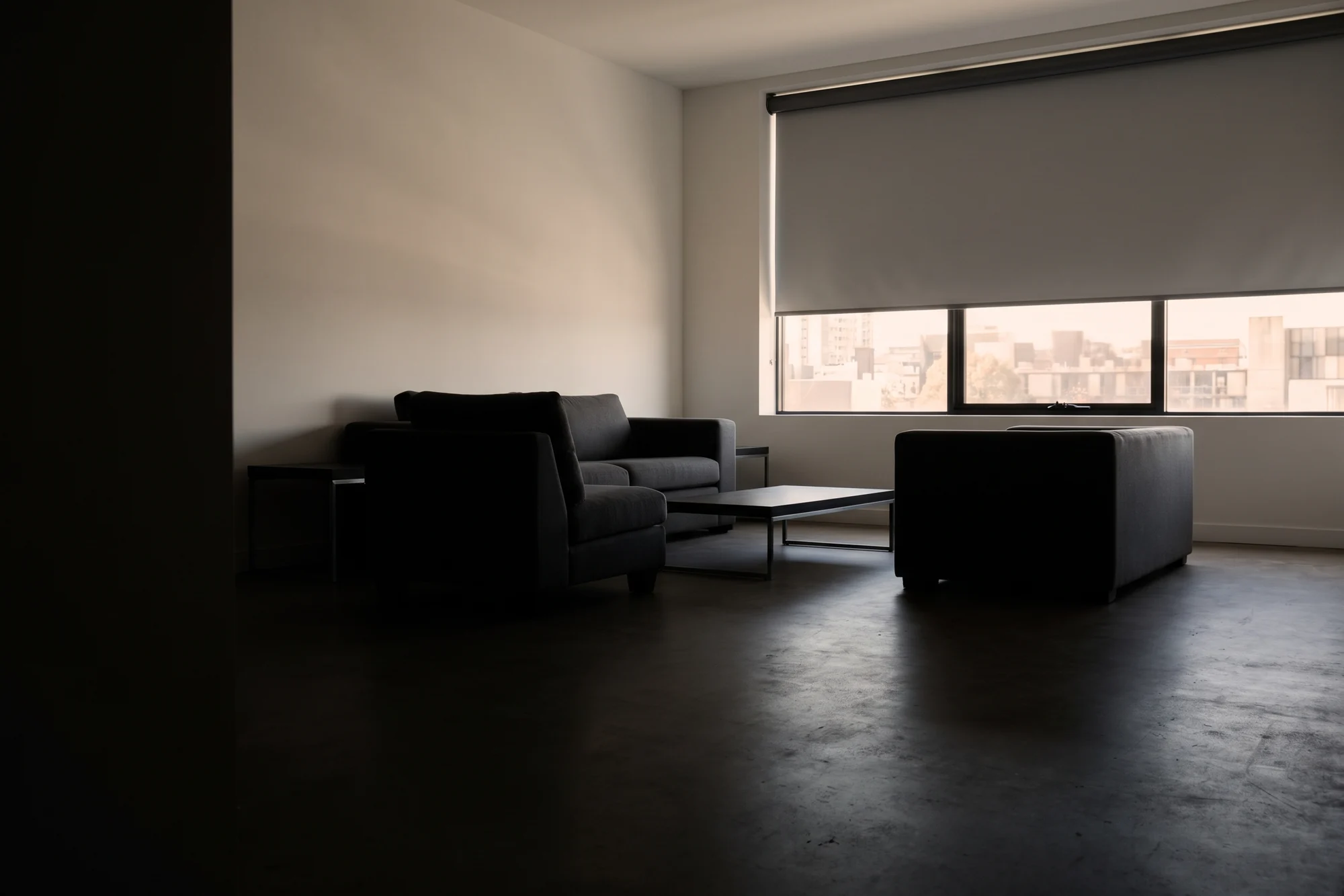 A blockout roller blind half drawn across a wide living-room window in afternoon light