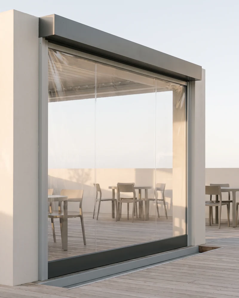 A clear PVC caf&eacute; blind running in side tracks across a terrace opening