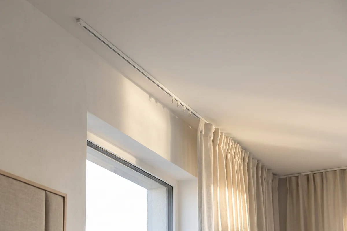 A slim white curtain track fixed to the ceiling, its runners carrying the curtain heading