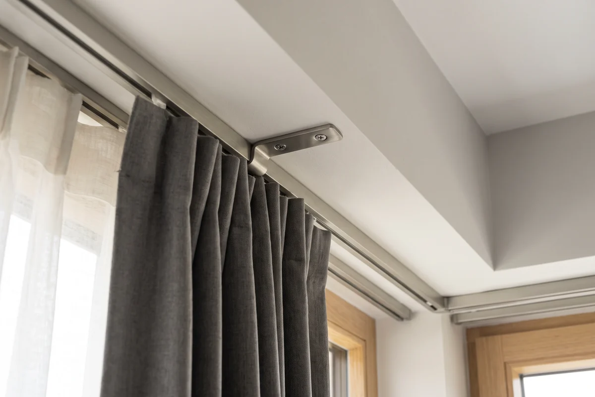 A curtain track bracket fixed into a ceiling above a window