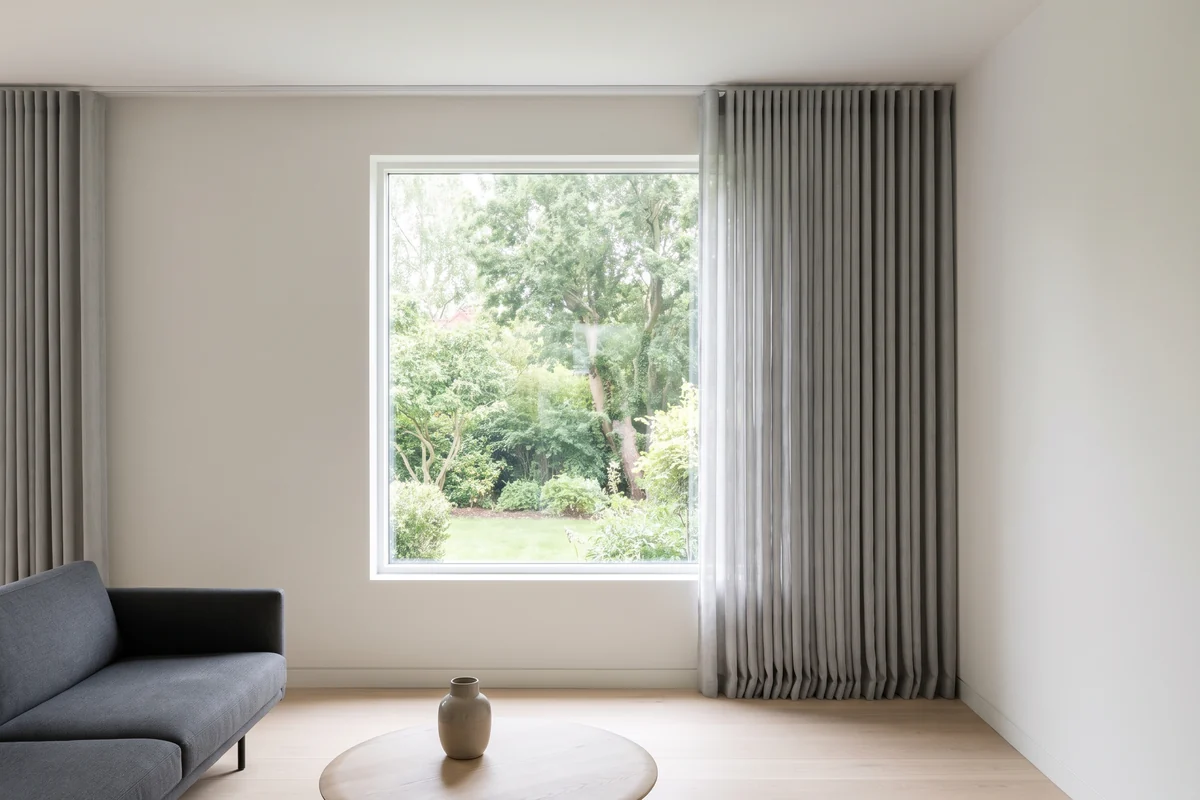 A ceiling curtain track running well past the window frame, with the open curtain stacked on the wall beside the glass