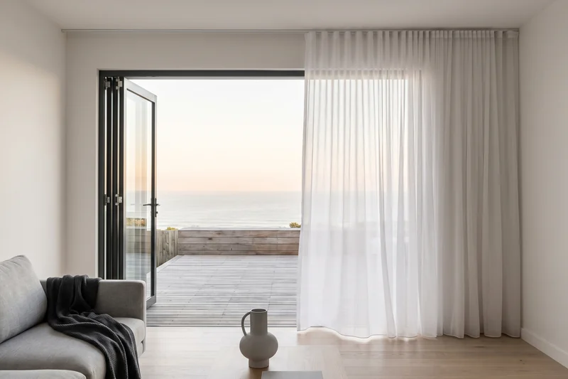 Floor-length sheer curtains stacked clear of open doors onto a coastal deck