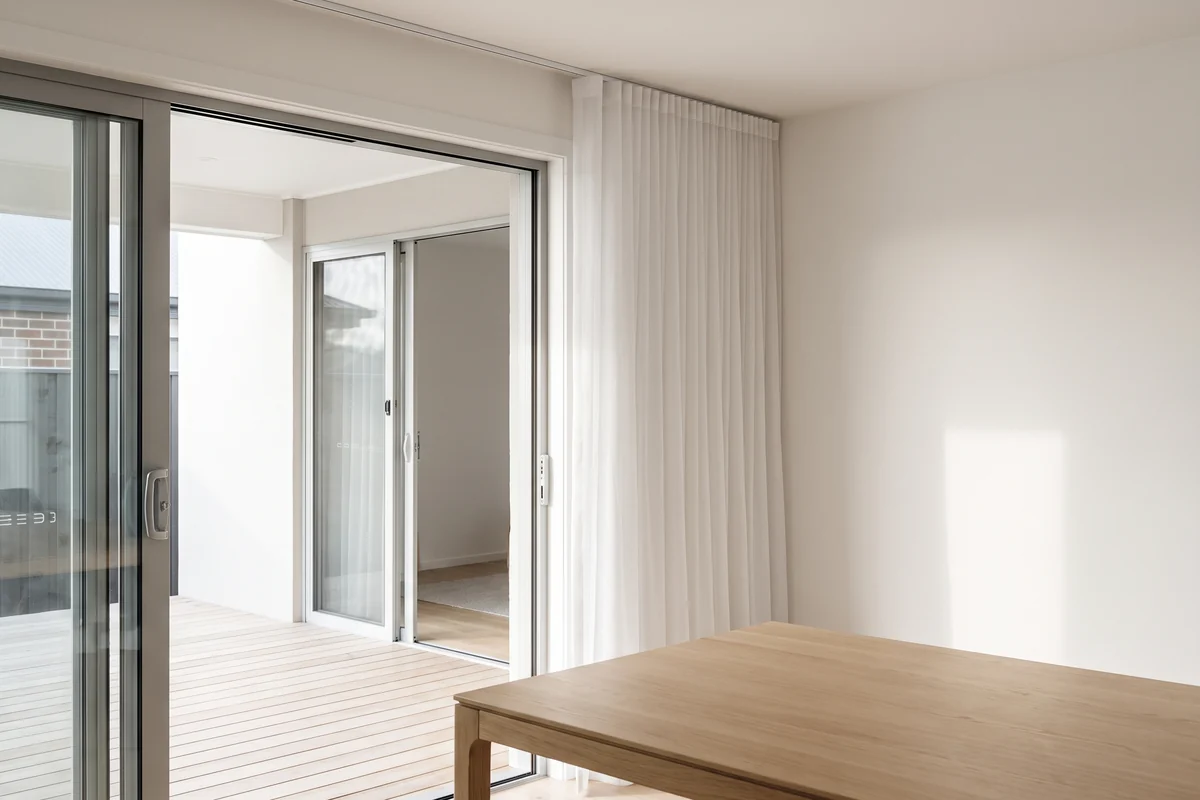 Sheer curtains stacked clear of an open sliding door between a dining room and a timber deck