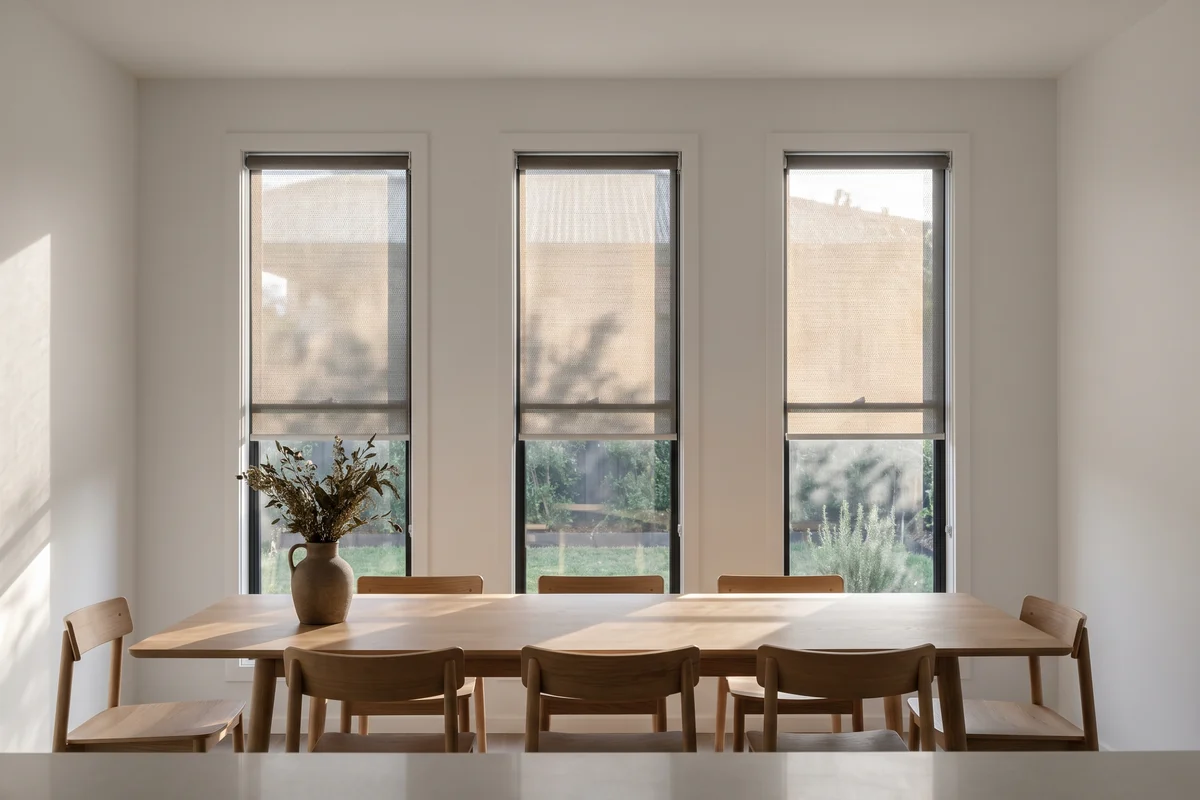 Sunscreen roller blinds half lowered across a row of dining room windows
