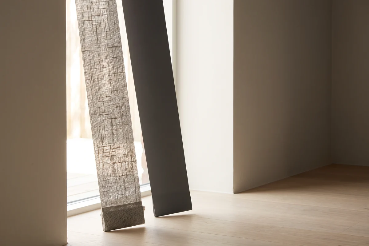 A woven fabric vertical slat and a solid PVC slat held against daylight