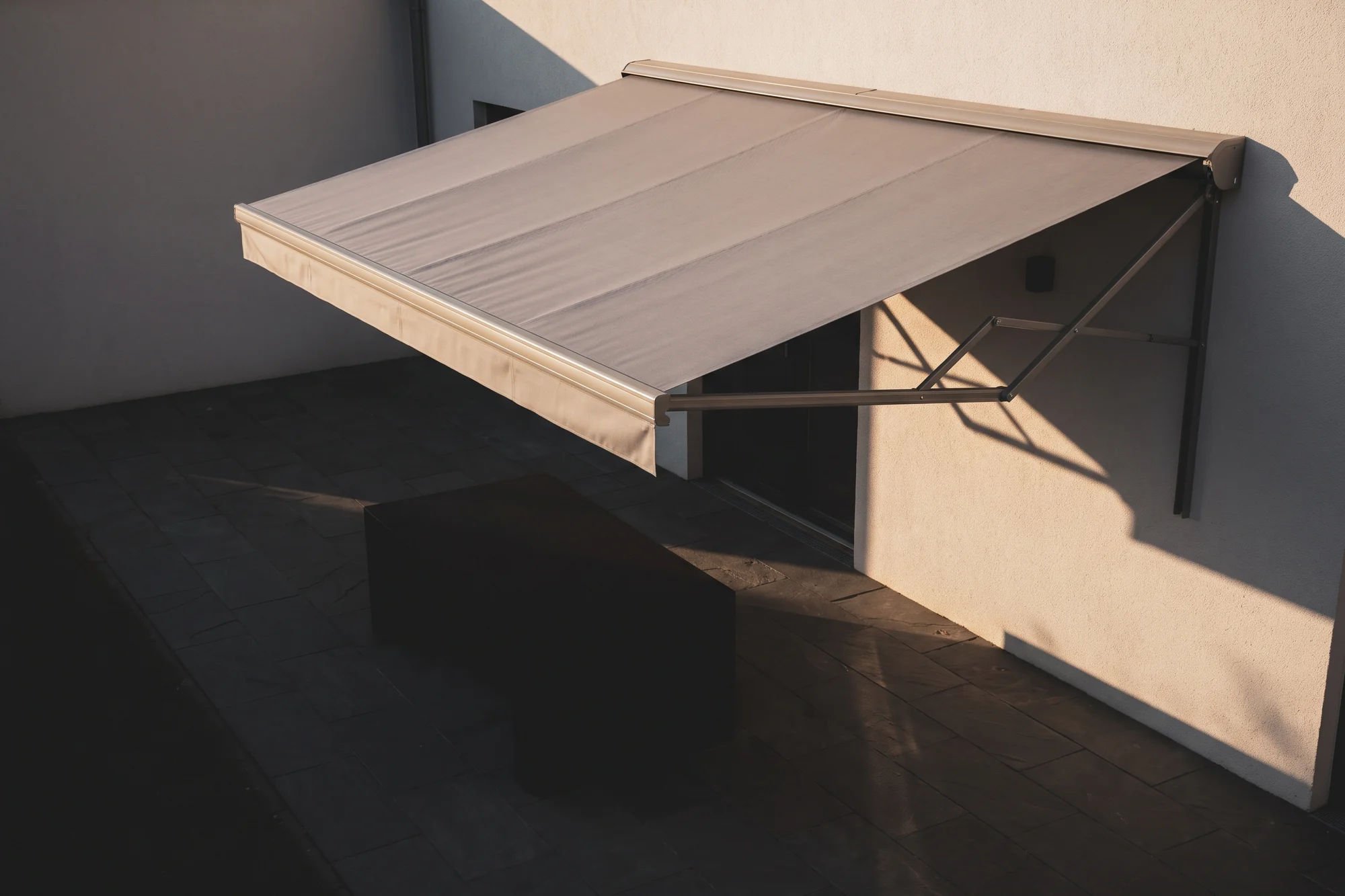 A folding arm awning extended over a paved courtyard in afternoon sun