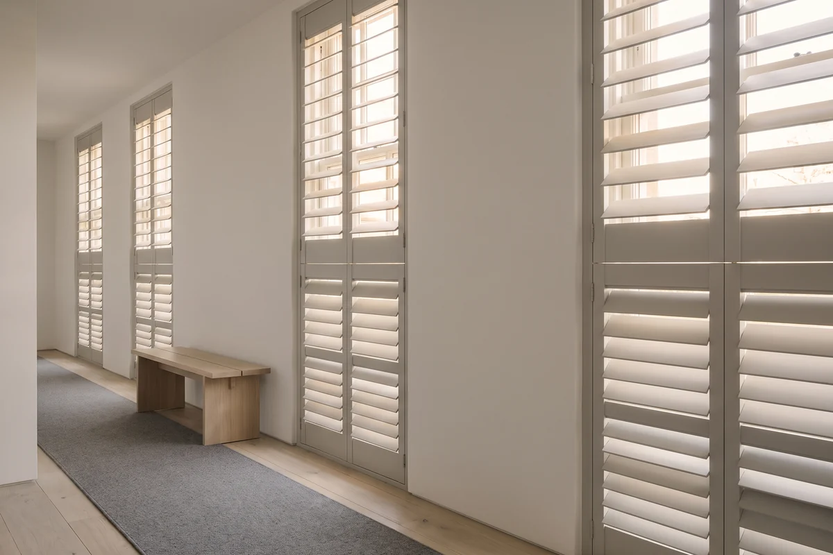 A hallway lined with tall windows fitted with louvred shutter panels