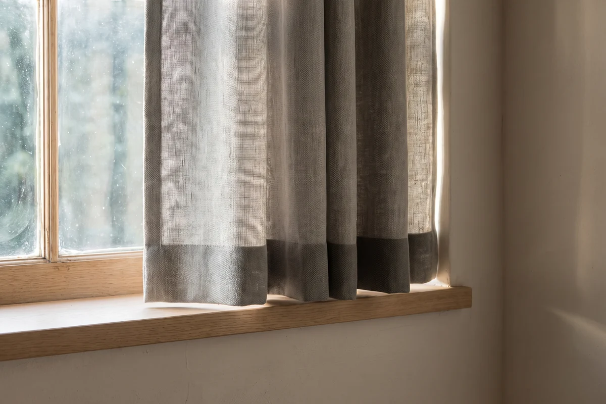 Lined curtains drawn across a sunlit window, daylight showing at the edges