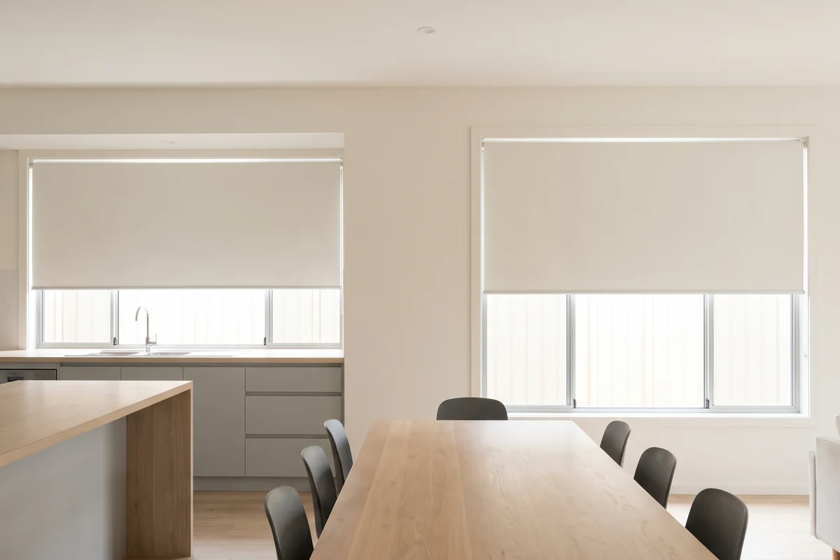 Matching roller blinds at one height across the kitchen and dining windows of an open-plan room
