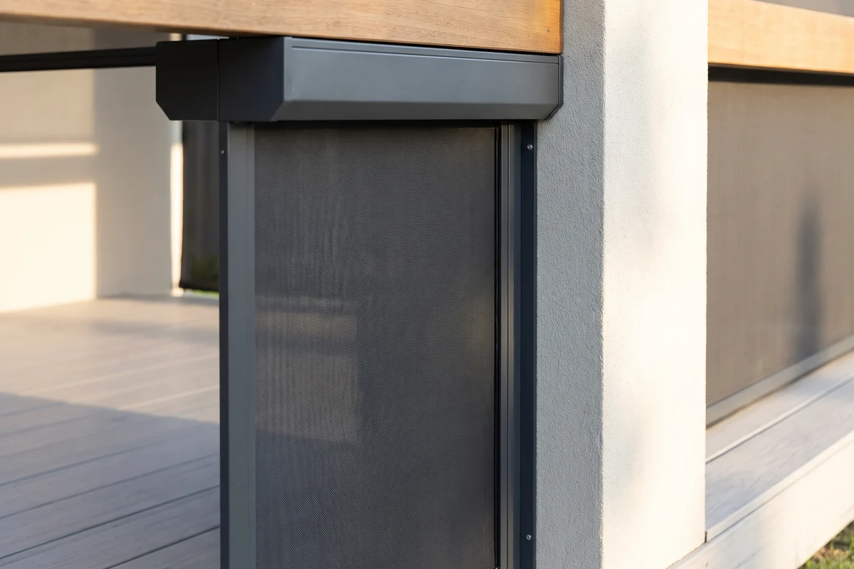 Charcoal mesh dropping from a graphite aluminium housing under a timber beam, its edge held in a side channel against a rendered column