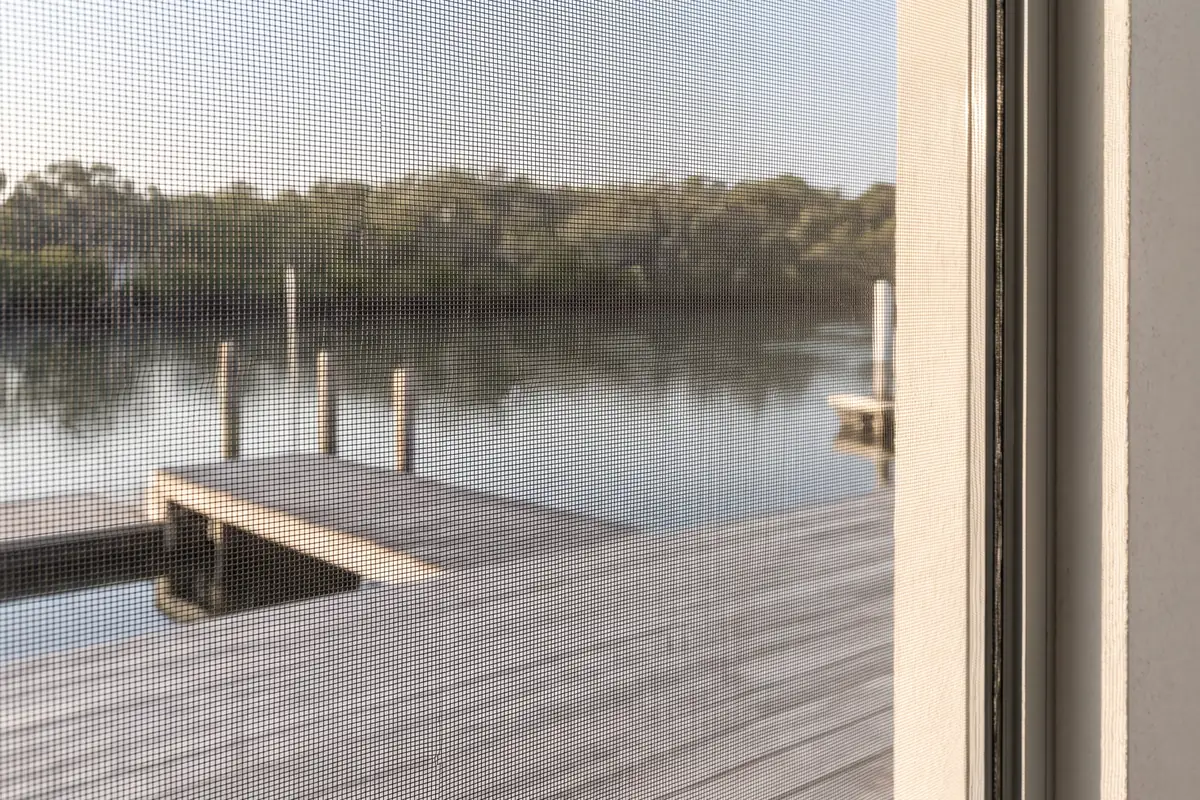 Close view of charcoal insect mesh, with a canal jetty and mangroves softly visible through the weave