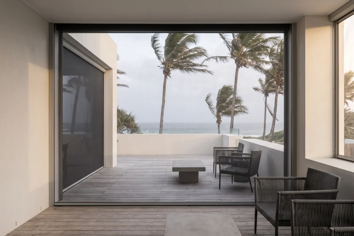 A fully lowered mesh screen held flat in its side channels while palm fronds bend in the wind beyond it