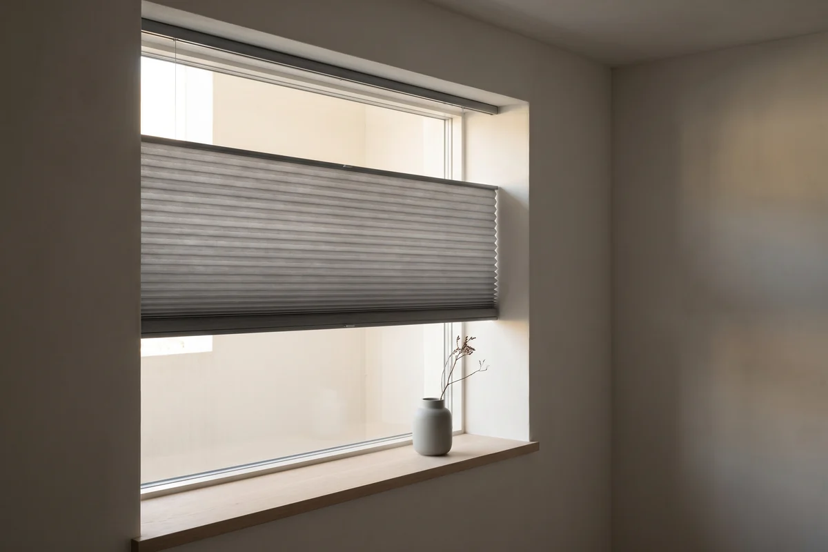 A pleated blind drawn partway down a window in a neutral-toned room