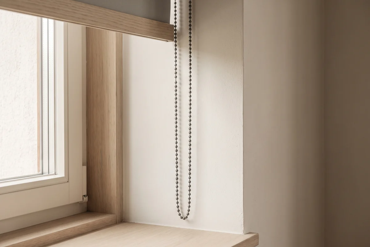 The side control chain of a roller blind running down beside a window frame