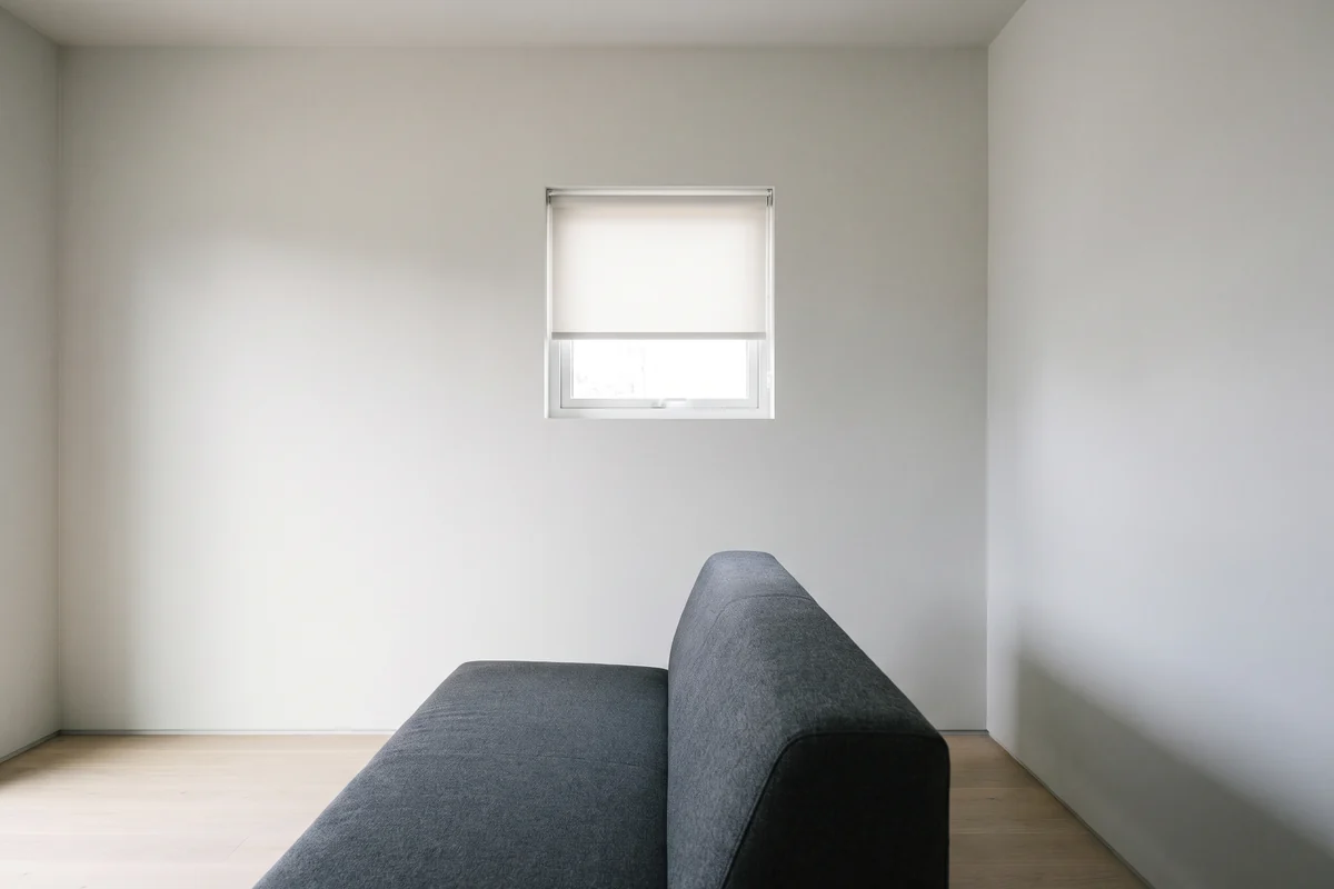 A small living room window above a sofa fitted with a roller blind instead of curtains