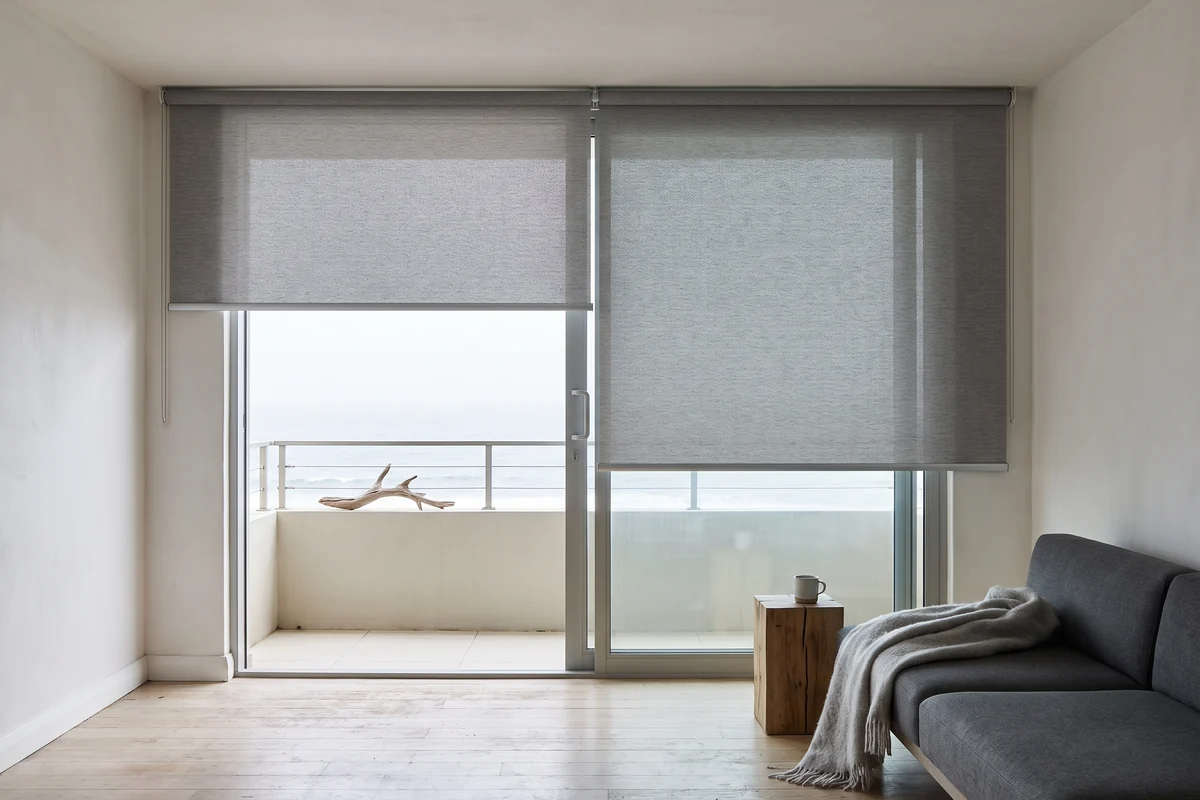 Two roller blinds hung level across a wide balcony opening above the sea