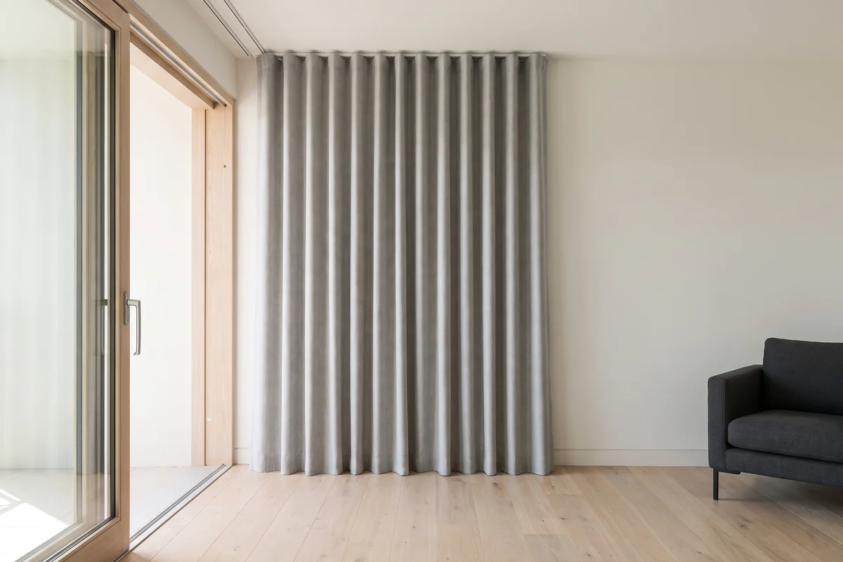 Floor-length S-fold curtains hanging in even waves from a runnered ceiling track beside an open sliding door