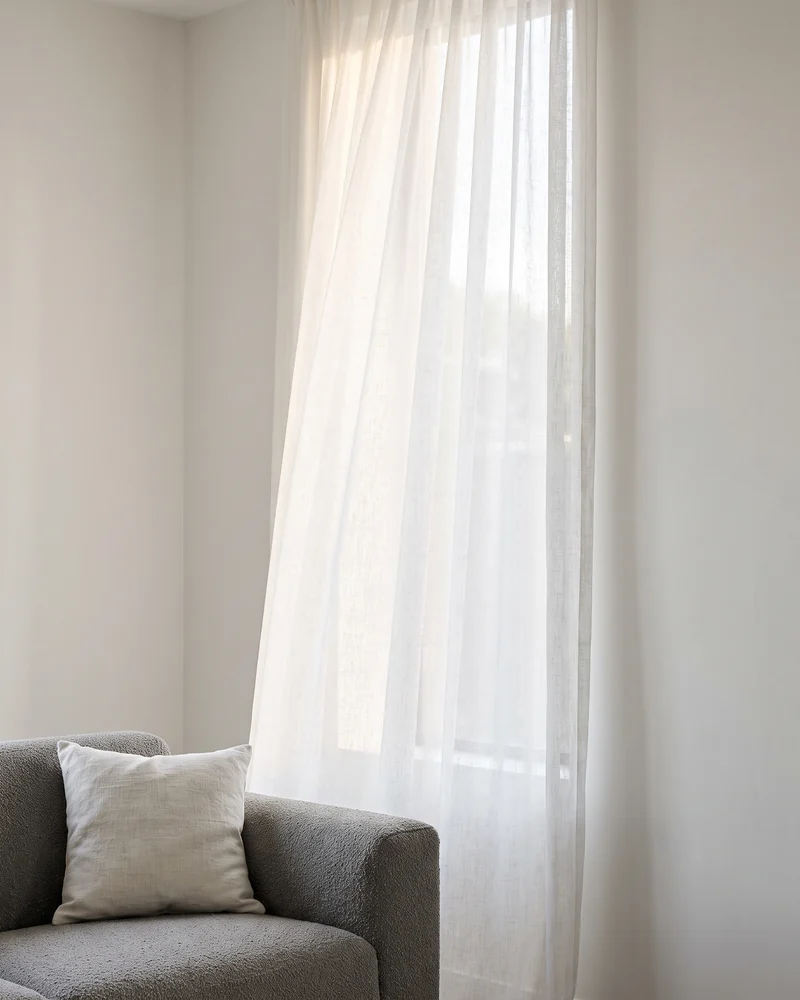 Sheer curtains diffusing daylight beside a sofa