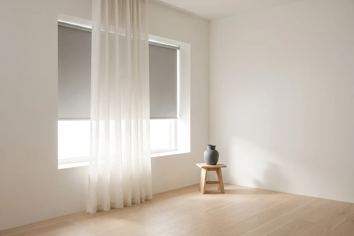 A sheer curtain hanging in front of a roller blind at the same window