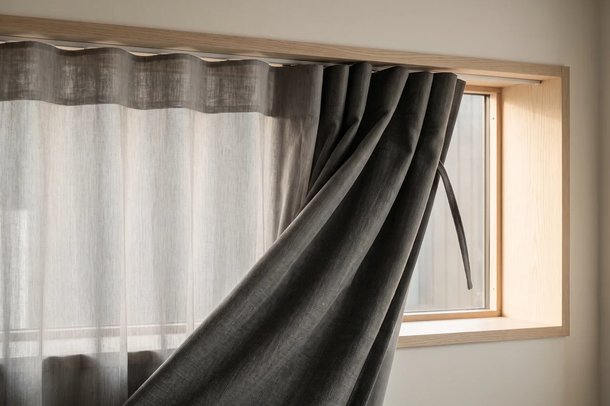 A sheer curtain drawn across a window with a blockout curtain stacked back beside it