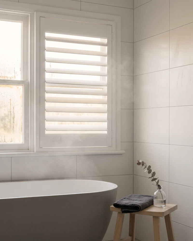 Shutters at a bathroom window above a bath, louvres tilted up for daylight without a sightline