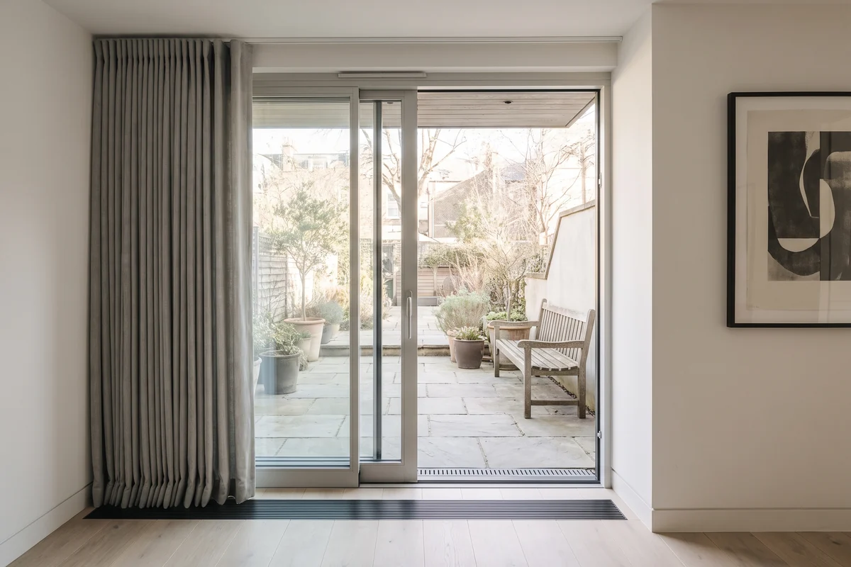 A sliding glass door standing open onto a garden, with the covering stacked clear of the opening