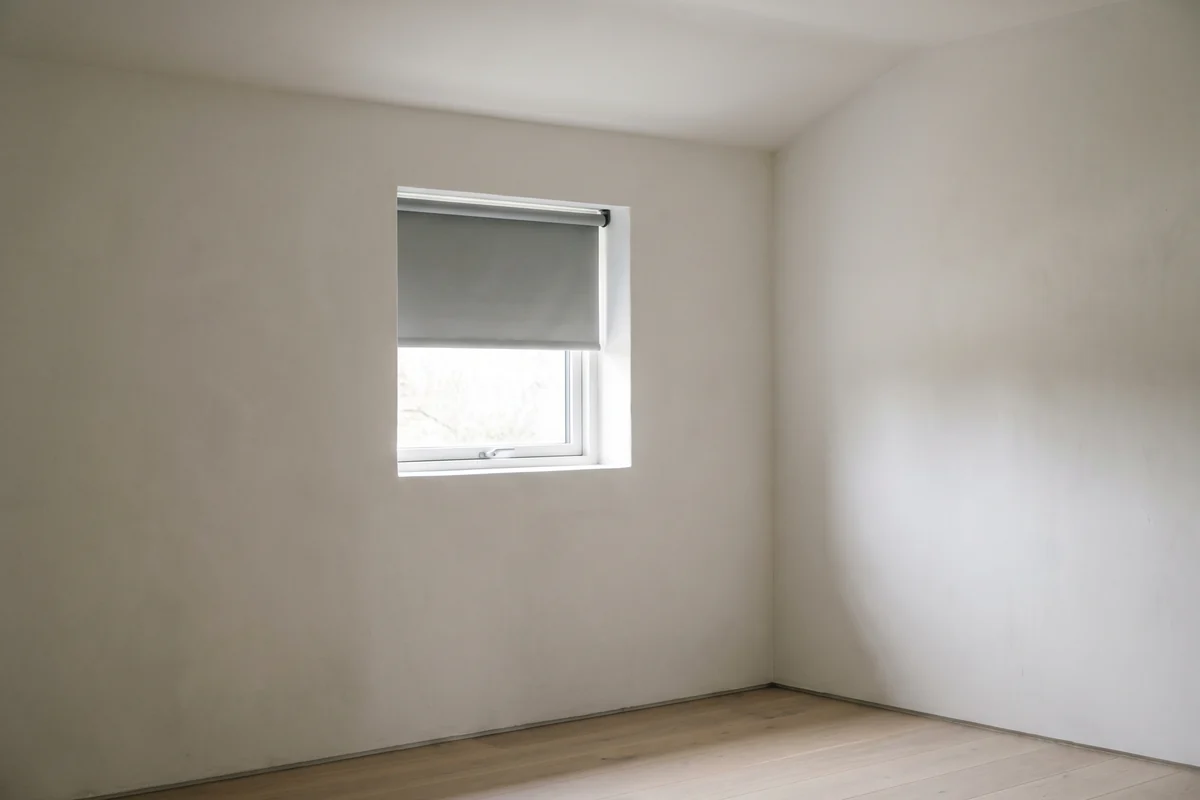A small square window fitted with a plain roller blind rather than curtains