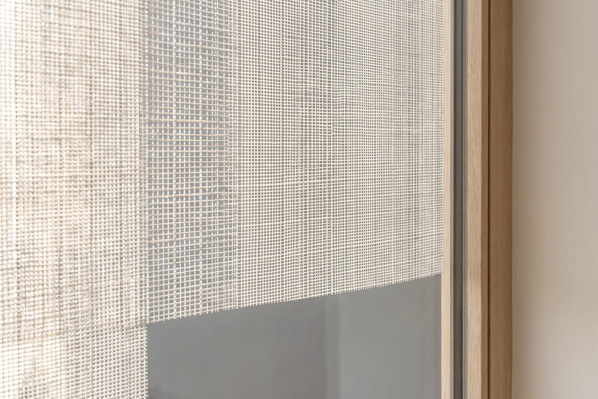Sunscreen blind fabric backlit by daylight, the open weave visible against the glass