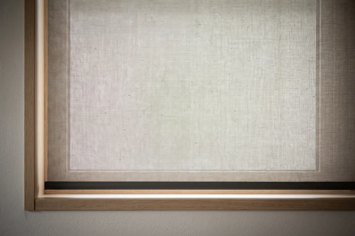 The finely woven fabric of a sunscreen roller blind seen close up against daylight