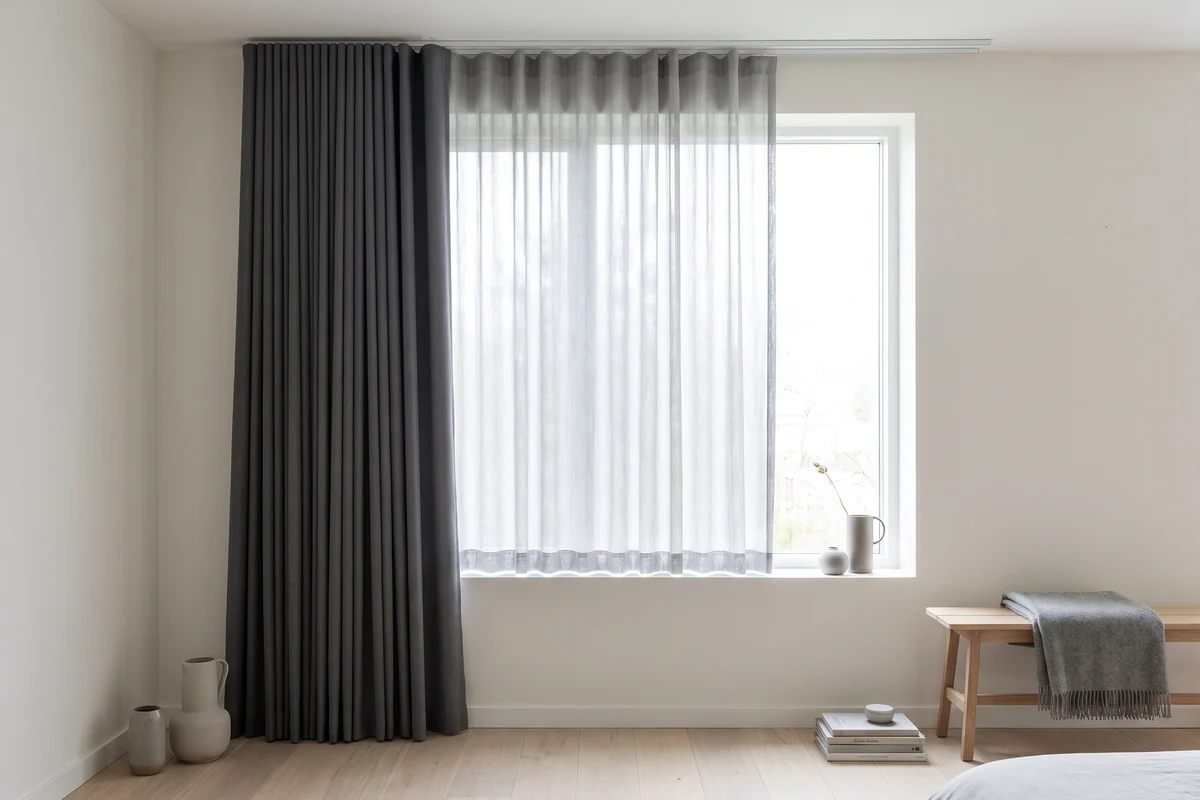 Bedroom window with a sheer curtain hanging behind a heavier blockout curtain on a double track