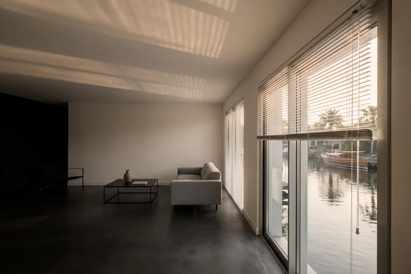 Aluminium venetian blind half raised over tall canal-front glass in late afternoon light