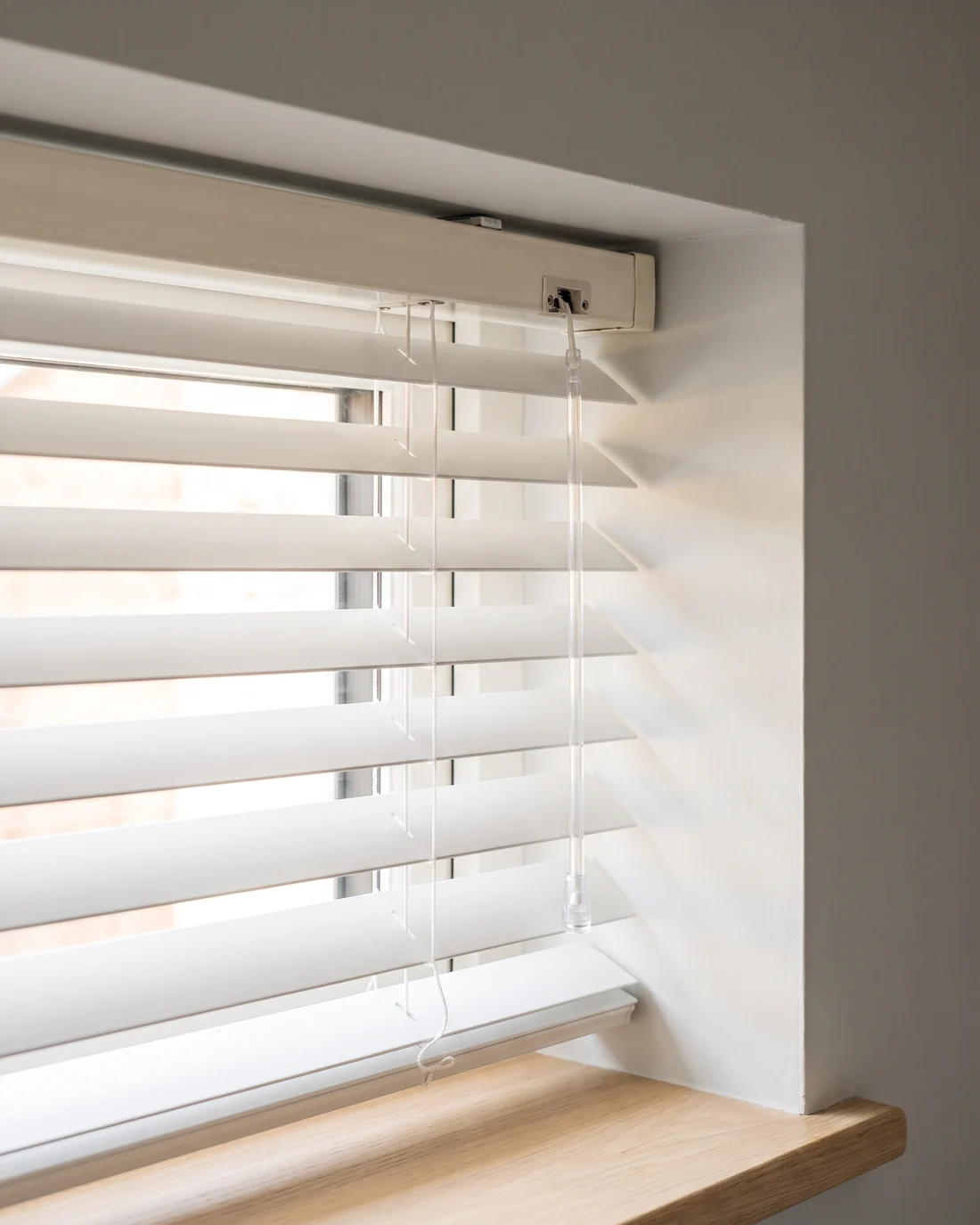 The headrail, tilt wand and ladder cord at the top corner of an aluminium venetian blind