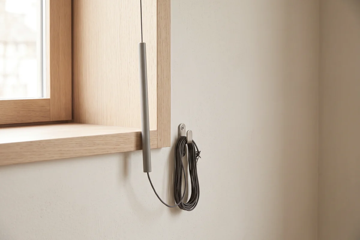 A tilt wand hanging beside a venetian blind with the cord held on a wall cleat