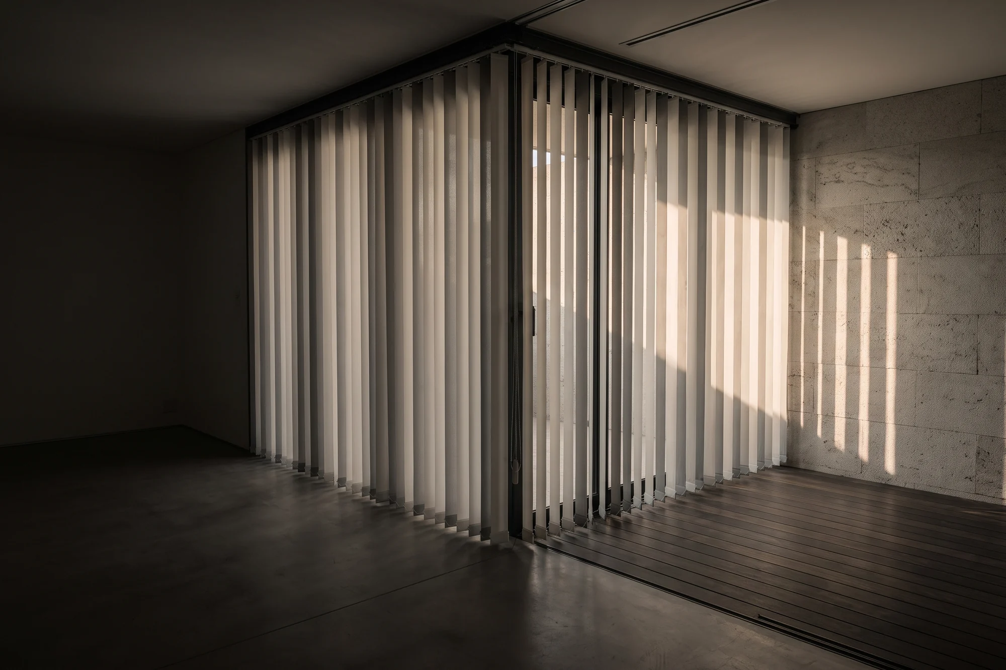 Vertical blinds drawn across a wide sliding door in a sunlit living room