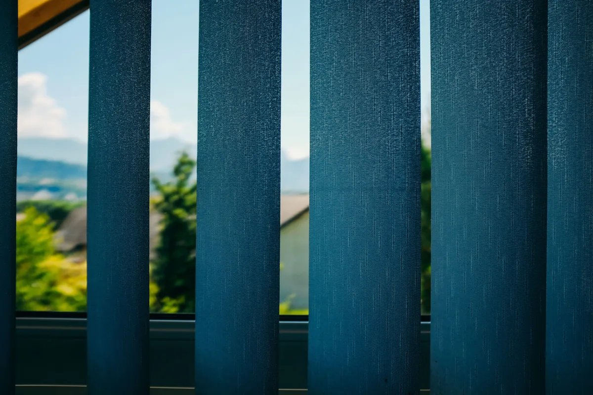 Vertical blind louvres angled open, showing the garden beyond