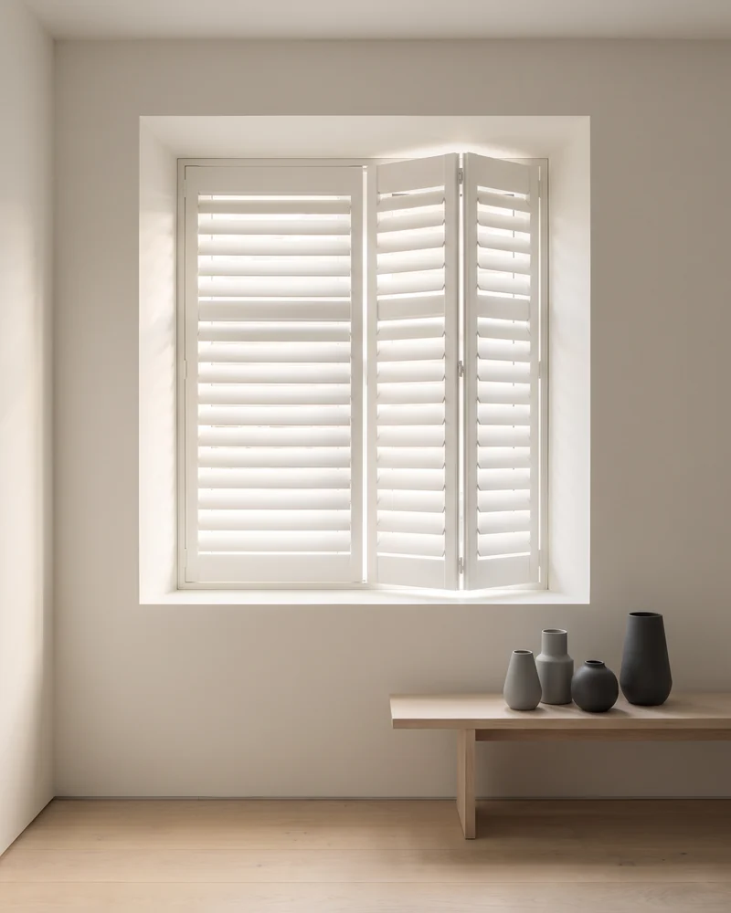 White interior shutters with louvres angled part open inside a window reveal