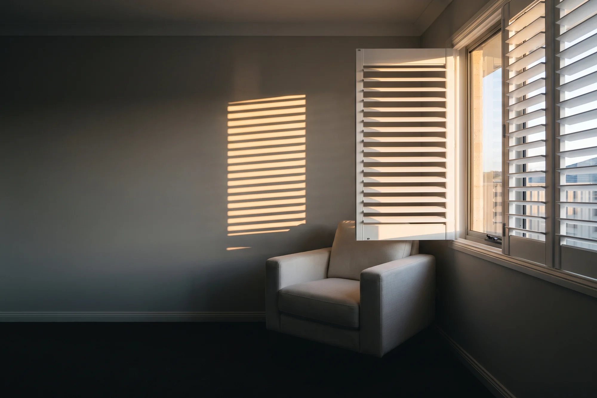 White polymer window shutters half open across a living-room window