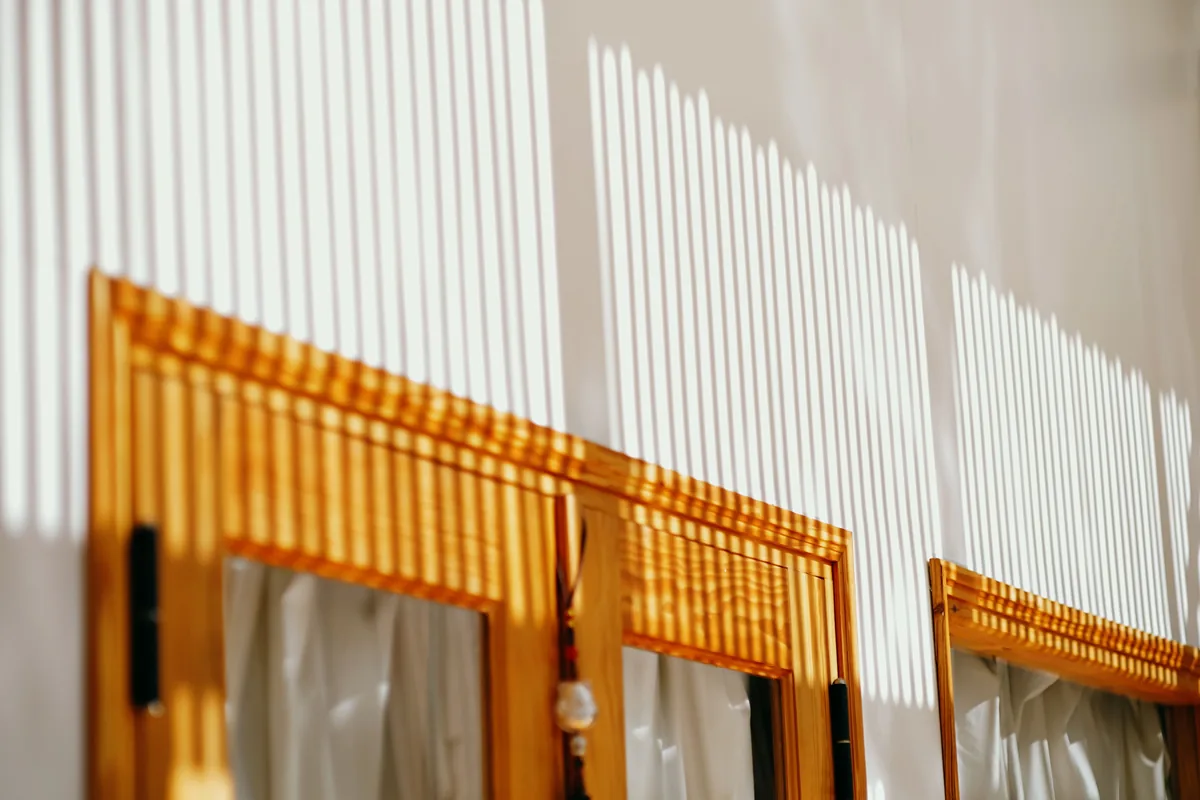 Louvre shadows cast across an interior wall by afternoon sun through a shutter