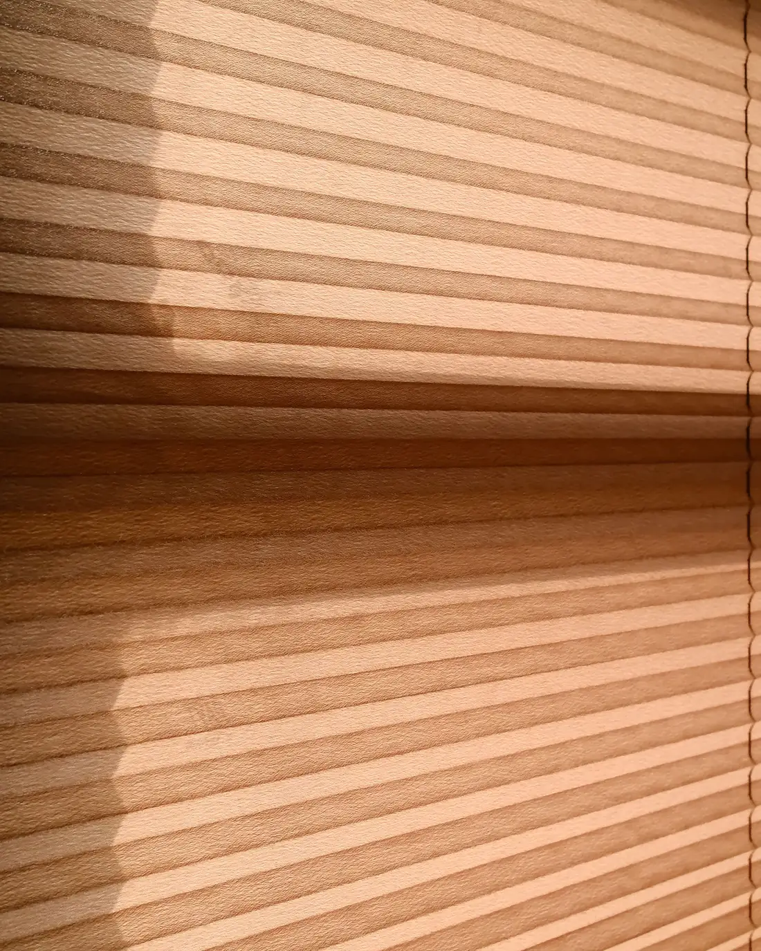 Afternoon sun and shadow falling across a pleated blind