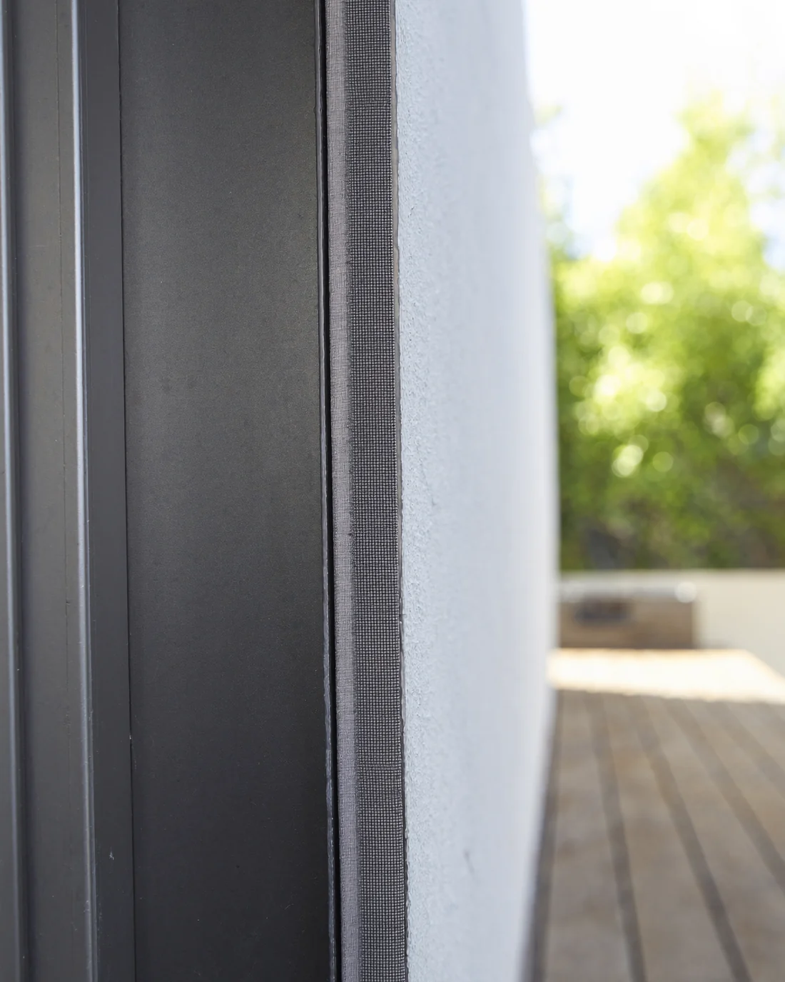 The mesh fabric edge of an outdoor blind zipped into its aluminium side channel